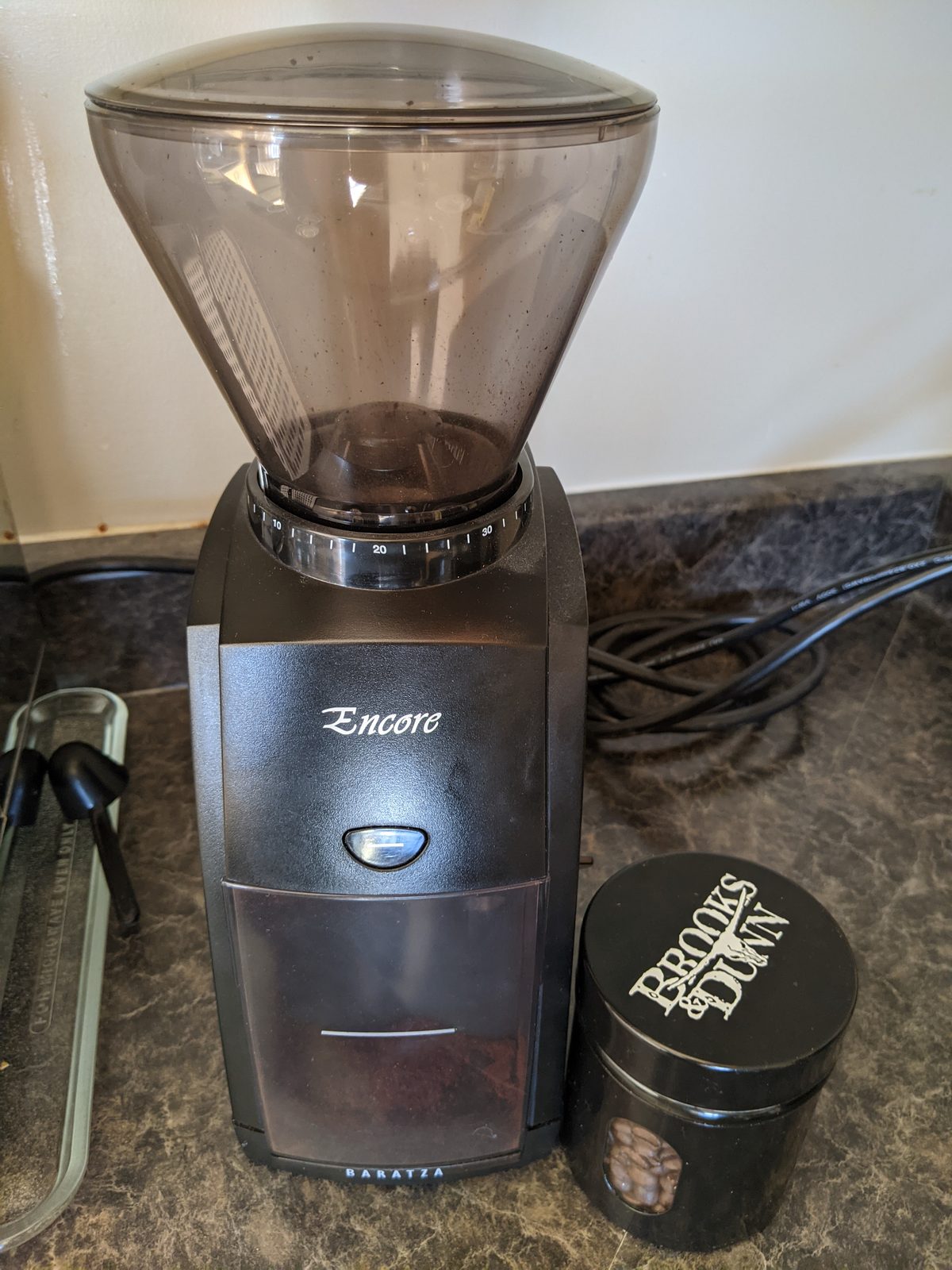 A burr coffee grinder on a kitchen counter beside a bean canister